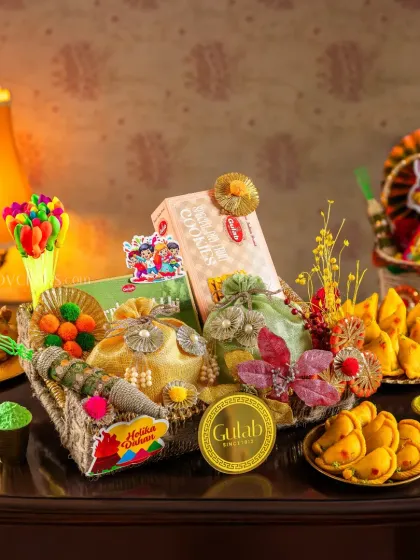 A dark, moody shot of a Holi hamper, with traditional sweets and snacks arranged on a vintage table.