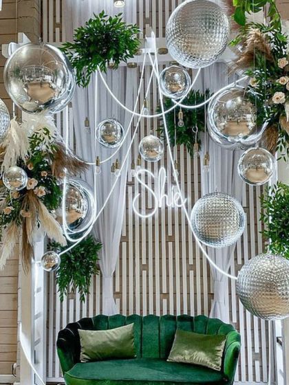 A chic and modern photo spot. We combined a white slatted backdrop with a green velvet sofa, a custom neon sign, and hanging disco balls with pampas grass for a unique, boho-glam vibe.