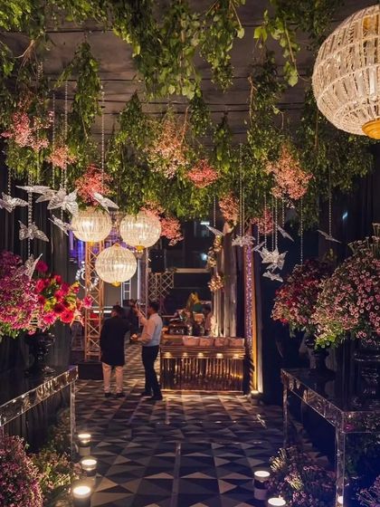 A different perspective of the enchanted forest walkway, showing the guest's view as they enter. The path is lined with candles and large floral bouquets, leading towards the main event area.