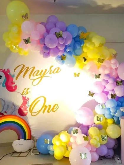 A unicorn and rainbow themed first birthday party. The decor features a custom backdrop, a unicorn cutout, and a pastel balloon arch.