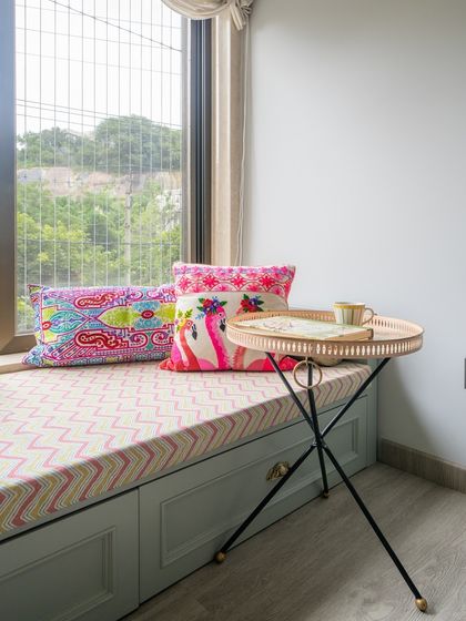 To create a vibrant reading nook in this Jubilee Hills bedroom, I used colorful handpicked textiles for the window seating. The space is perfect for cozying up with a book while enjoying the lush green view, completed by a hand-painted folding tray table.