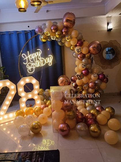 A sophisticated backdrop for a 28th birthday, featuring a half-arch of nude, chrome, and rose gold balloons. The clear pedestal and marquee numbers add to the modern aesthetic.