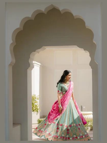 A bride framed by history. The elegant archway provides a perfect, natural frame for this shot, highlighting the flow and design of her mint and pink lehenga as she moves through the space.