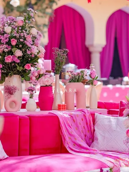 A cozy corner of the lounge, where a plush pink sofa is adorned with textured cushions and surrounded by an abundance of floral arrangements in modern vases.