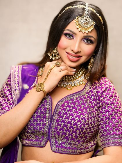 A smiling bride-to-be in a vibrant purple outfit. The makeup is kept bright and cheerful, with a pop of purple on the eyes and a radiant smile.