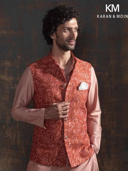 This terracotta embroidered Nehru jacket, layered over a blush-toned kurta set, is a poetic blend of tradition and tailored modernity. The all-over floral threadwork in earthy tones is perfect for the man who doesn’t just wear tradition, he redefines it.