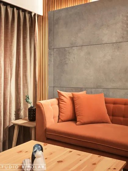 This living room corner is all about the power of contrast. A vibrant orange sofa pops against a cool, grey concrete-paneled wall, while a black-and-white patterned rug adds another layer of graphic interest.