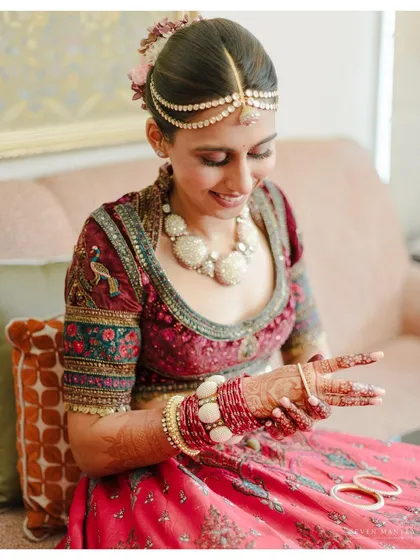 The final touches. This candid shot captures the bride's happiness as she puts on her bangles, a small but significant part of her wedding day ritual. Her jewel-toned blouse adds a touch of classic royalty.
