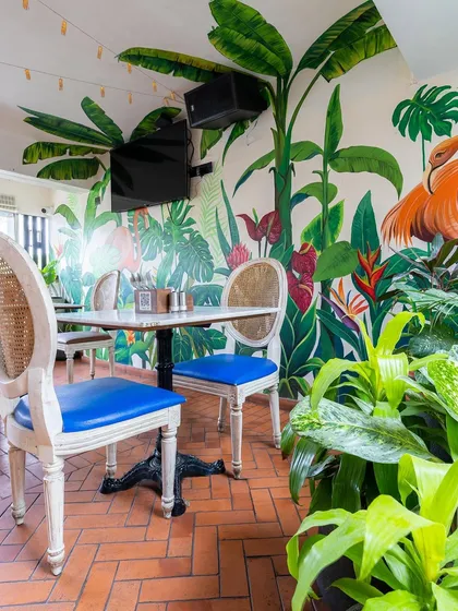 The tropical mural extends across the dining area, creating an immersive and colorful backdrop. Paired with natural brick flooring and classic chairs, the space feels both whimsical and grounded.