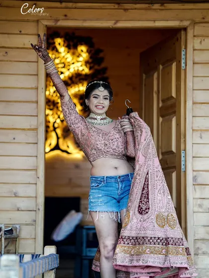 A fun and unconventional bridal portrait. The bride, in her blouse and shorts, joyfully holds up her wedding lehenga, ready for the big day.