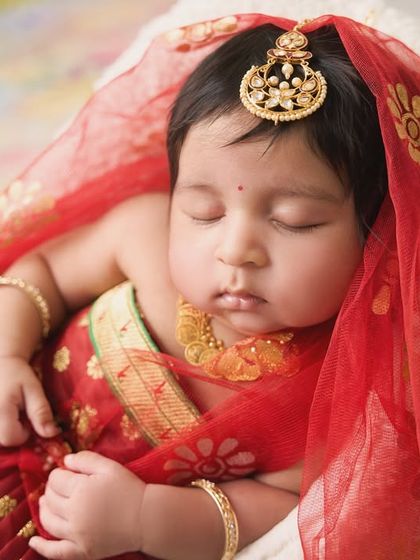 Another beautiful angle of the newborn goddess, highlighting the rich red fabric of her outfit and her peaceful sleep.