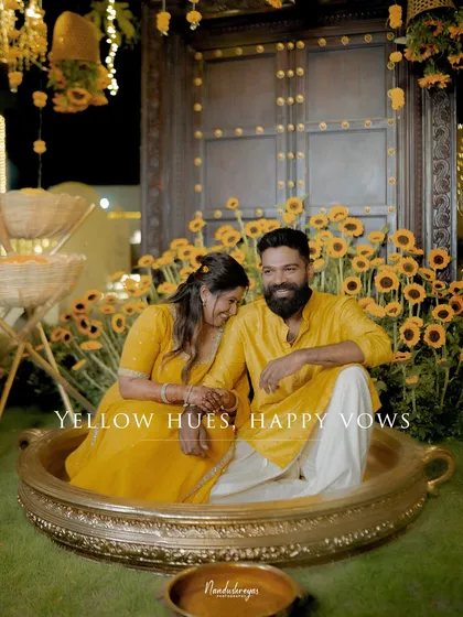 A joyful couple, dressed in vibrant yellow for their Haldi ceremony, shares a laugh while sitting in a giant decorative teacup. This photo captures the fun, color, and unique personal touches of traditional wedding celebrations.