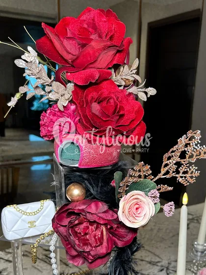 A close-up of a dramatic floral centerpiece with deep red roses and Chanel-inspired accents, perfect for a high-fashion themed event.
