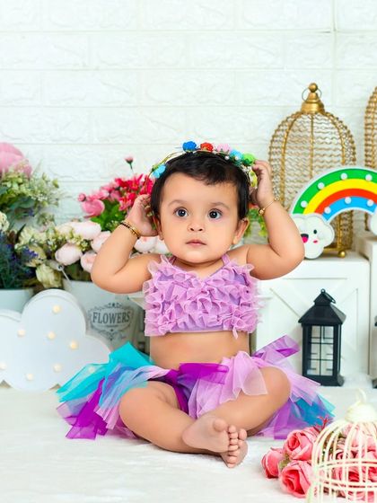 A moment of adorable concentration as this little one places a floral crown on her head. The rainbow prop adds a touch of whimsy.