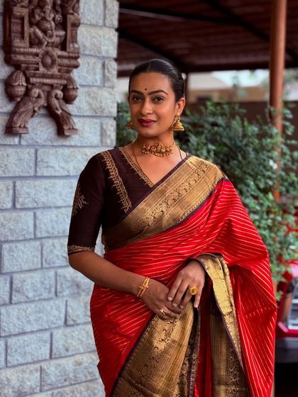 A full-length view of a client looking poised and elegant. The dark blouse provides a beautiful contrast to her bright red silk saree.