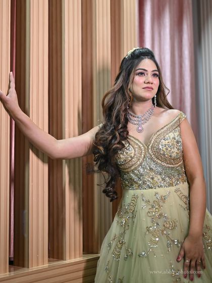 A model posing in a light green off-shoulder gown with heavy silver and gold embroidery. The delicate diamond necklace completes this glamorous reception look.