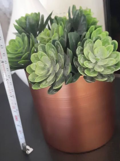 A beautiful copper-finished metal pot with an artificial succulent. I'm showing the size here with a measuring tape; it's a great medium-sized pot for a side table or shelf.