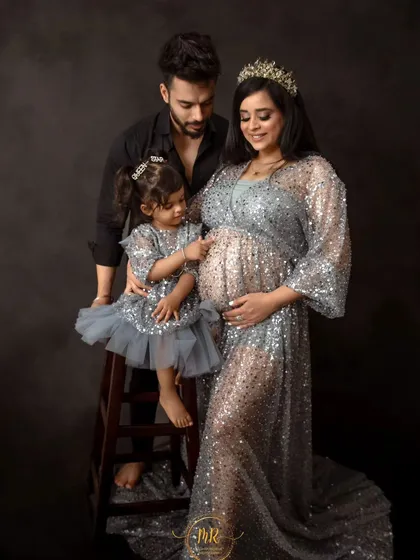 A sweet family moment. The daughter, standing on a stool, reaches out to touch her mother's baby bump as the father looks on, creating a heartwarming scene.