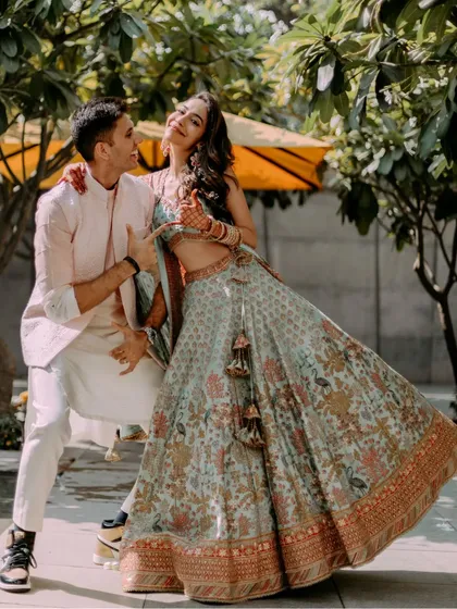 A joyful and candid portrait of the couple during their outdoor Mehendi or Haldi event, sharing a laugh in a sunlit garden setting.