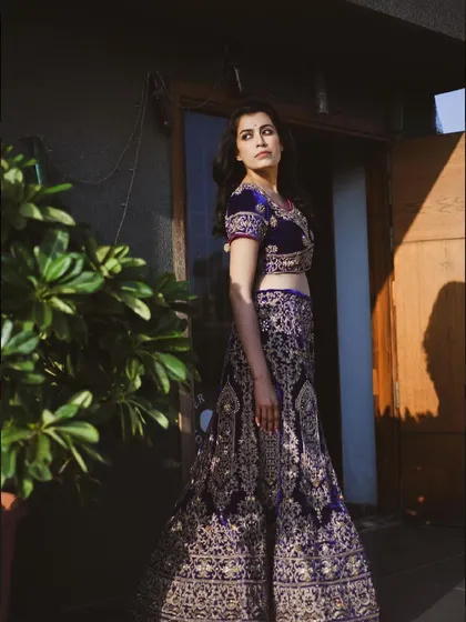A full-length shot of a woman in a stunning lehenga, taken outdoors. The natural light highlights the intricate details of the embroidery.