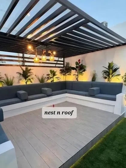 A modern and clean rooftop lounge design. The space is defined by a sleek black pergola over a light-colored wood deck, with built-in L-shaped seating.
