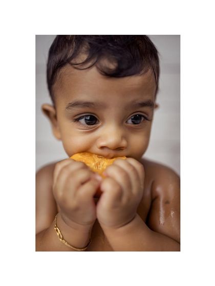 An adorable close-up of a baby boy's face as he bites into a juicy orange slice during his fruit bath photoshoot. This shot perfectly captures a moment of pure sensory discovery.