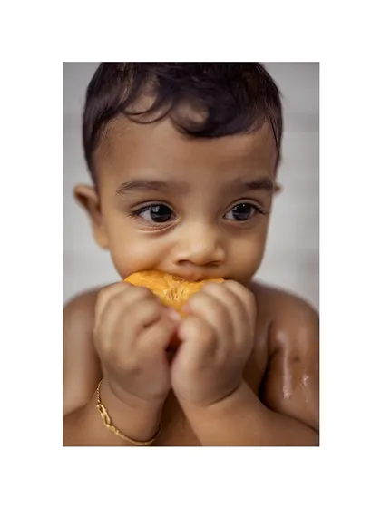 An adorable close-up of a baby boy's face as he bites into a juicy orange slice during his fruit bath photoshoot. This shot perfectly captures a moment of pure sensory discovery.