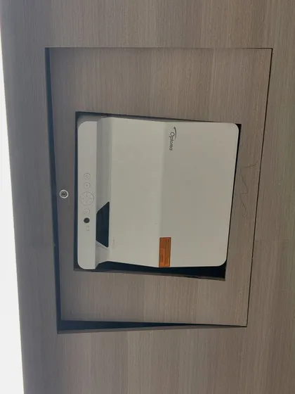 A close-up of the custom-built niche housing the Optoma AZH430UST projector. This clean installation keeps the hardware out of the way, preventing clutter on the conference table and protecting the equipment.