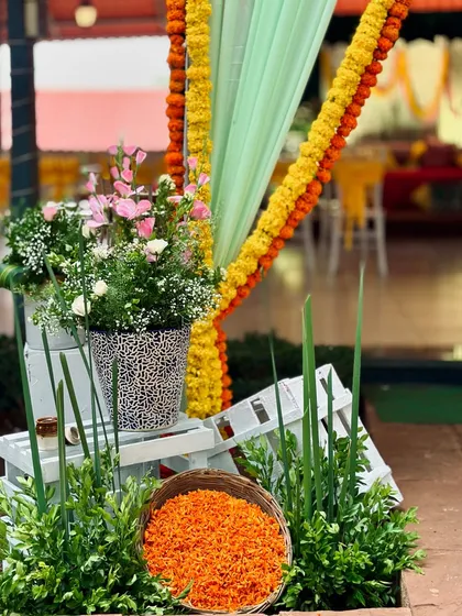 A decorative corner at a Mehendi event, featuring flower arrangements on white wooden crates and marigold garlands.