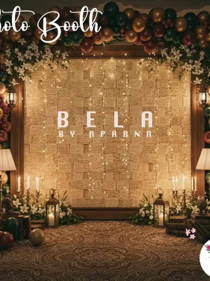 A cozy and elegant photo booth with a stone-textured wall and warm fairy lights. The space is framed by a balloon arch in rich, earthy tones and decorated with vintage lamps and books to create an inviting atmosphere.