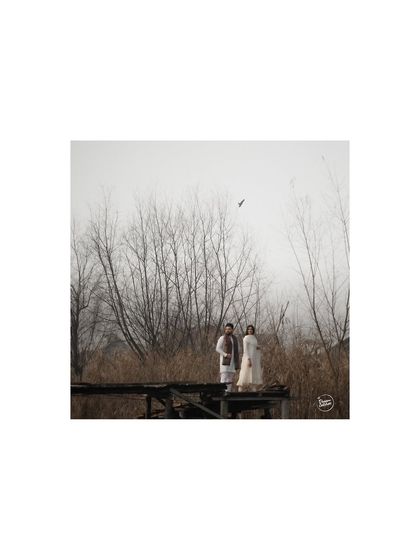 A wide shot of a couple on a rustic bridge in Kashmir, with a bird flying overhead. We often incorporate elements of nature to add a touch of serendipity and artistry to our compositions.