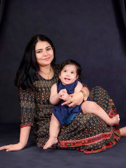 A mother and her happy baby girl seated against a dramatic black curtain backdrop. The contrast makes their smiles shine even brighter.