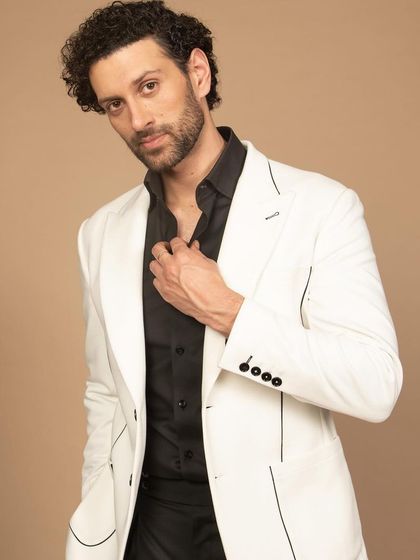 A crisp white blazer with fine black piping detail. Paired with a black shirt, this creates a sharp, high-contrast look that is both modern and timeless.