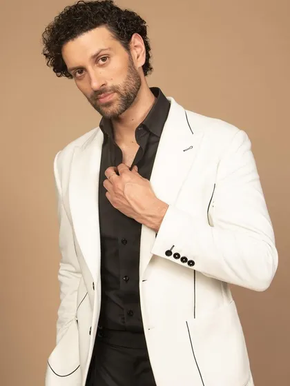 A crisp white blazer with fine black piping detail. Paired with a black shirt, this creates a sharp, high-contrast look that is both modern and timeless.