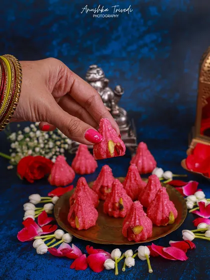 Rose-flavoured modaks, styled with fresh rose petals and jasmine flowers. The human touch, with bangles and henna, adds a beautiful cultural and personal element.