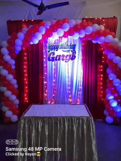 A classic birthday cake-cutting backdrop. The red and white balloon arch, combined with a custom 'Happy Birthday Gargi' sign and fairy lights, is a popular and festive choice.