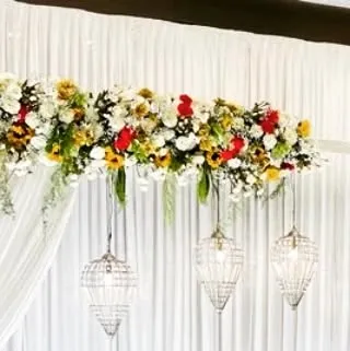 The top section of a wedding arch, showcasing the arrangement of mixed flowers and hanging crystal lanterns against a clean white drape.