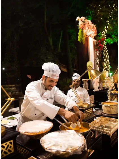 A smiling chef at a live Indian food counter, happily serving guests. My team's friendly and professional service is a key part of the experience.