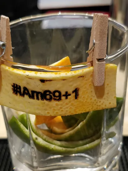 A close-up of the custom hashtag #IAm69+1 stamped onto an orange peel. This kind of detail is perfect for milestone birthdays and corporate events, making every drink shareable on social media.