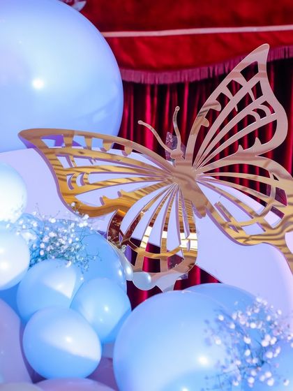 A close-up of a golden butterfly accent nestled among pastel blue balloons. These small, high-quality details add a touch of elegance and reinforce the magical fairy theme throughout the event space.