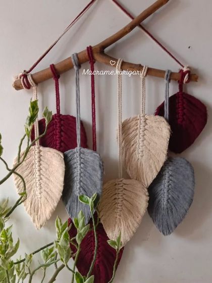 A macramé wall hanging featuring feathery leaves in maroon, grey, and beige. This piece brings a touch of nature-inspired art to your walls.