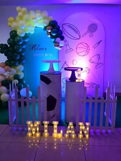 The full view of the 'Game On' sports theme, showing the custom backdrop, balloon arch, themed pedestals, and light-up marquee letters for the name.