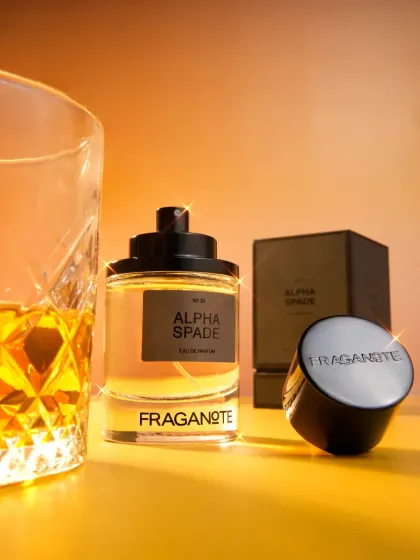A sophisticated shot of 'Alpha Spade' perfume next to a glass of whiskey, with a digital sparkle added for a touch of magic. We can add subtle post-production effects to enhance the premium feel.