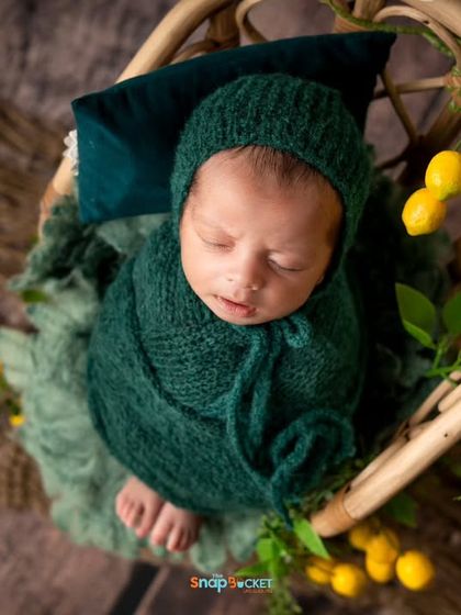 An overhead view of this newborn nestled in a round basket, surrounded by lemons. The contrast of the green wrap and yellow fruit creates a fresh and unique composition.