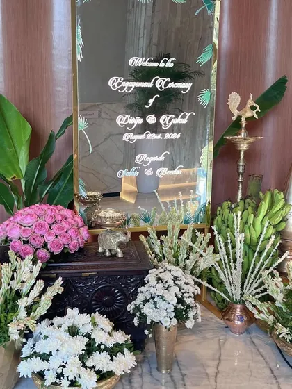 A personalized welcome mirror for the engagement ceremony. Surrounded by traditional flowers and brass elements, it’s a modern touch that blends seamlessly with classic decor.