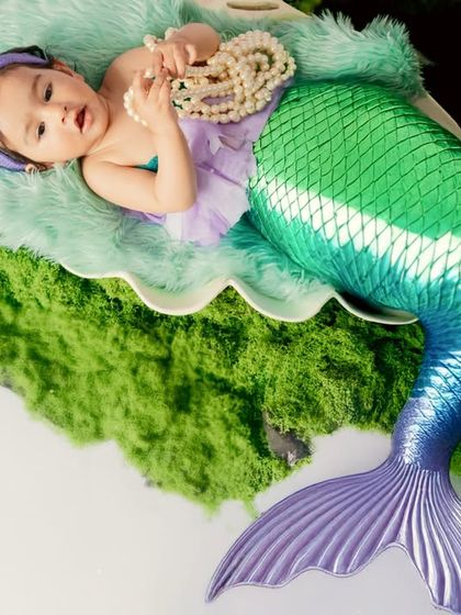 A magical mermaid newborn shoot. This tiny baby is dressed in a shimmering mermaid tail, resting peacefully in a giant seashell on a bed of green moss.