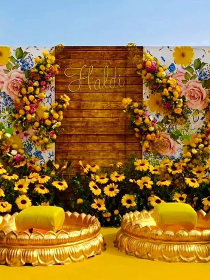 A rustic Haldi backdrop with a wooden panel and a frame of sunflowers and yellow roses. The golden urlis for seating add a touch of tradition.