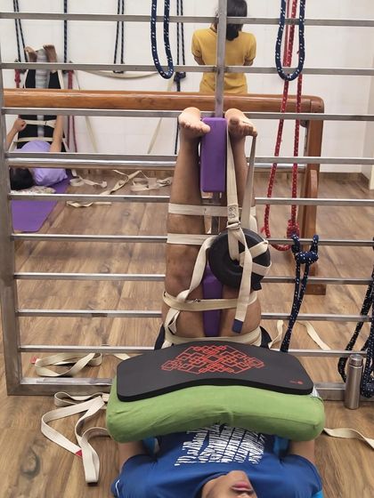 A student in a therapeutic setup for the legs using a stall bar, belts, blocks, and weights. This is highly effective for knee issues and creating space in the hip joints.