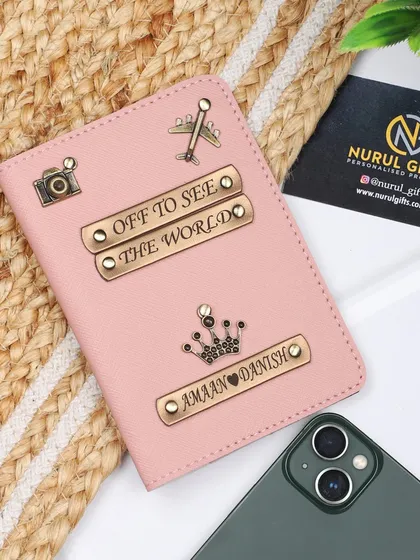 A beautiful pink passport cover, fully customized with two names, multiple charms like a camera and airplane, and the inspiring quote 'Off to see the world'.