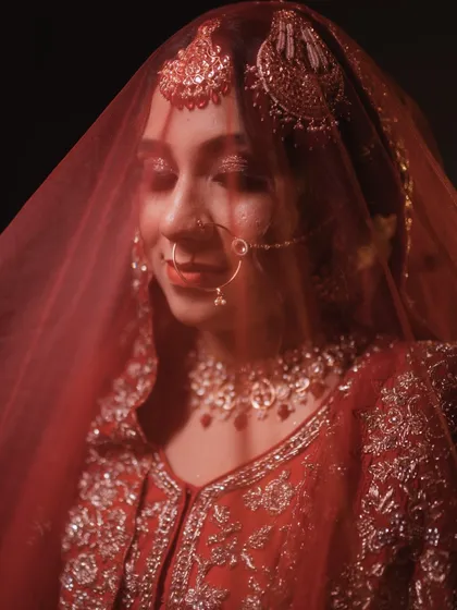 A bride is incomplete without her veil. This artistic shot through the red dupatta highlights the delicate jewelry and soft, glowing makeup underneath.